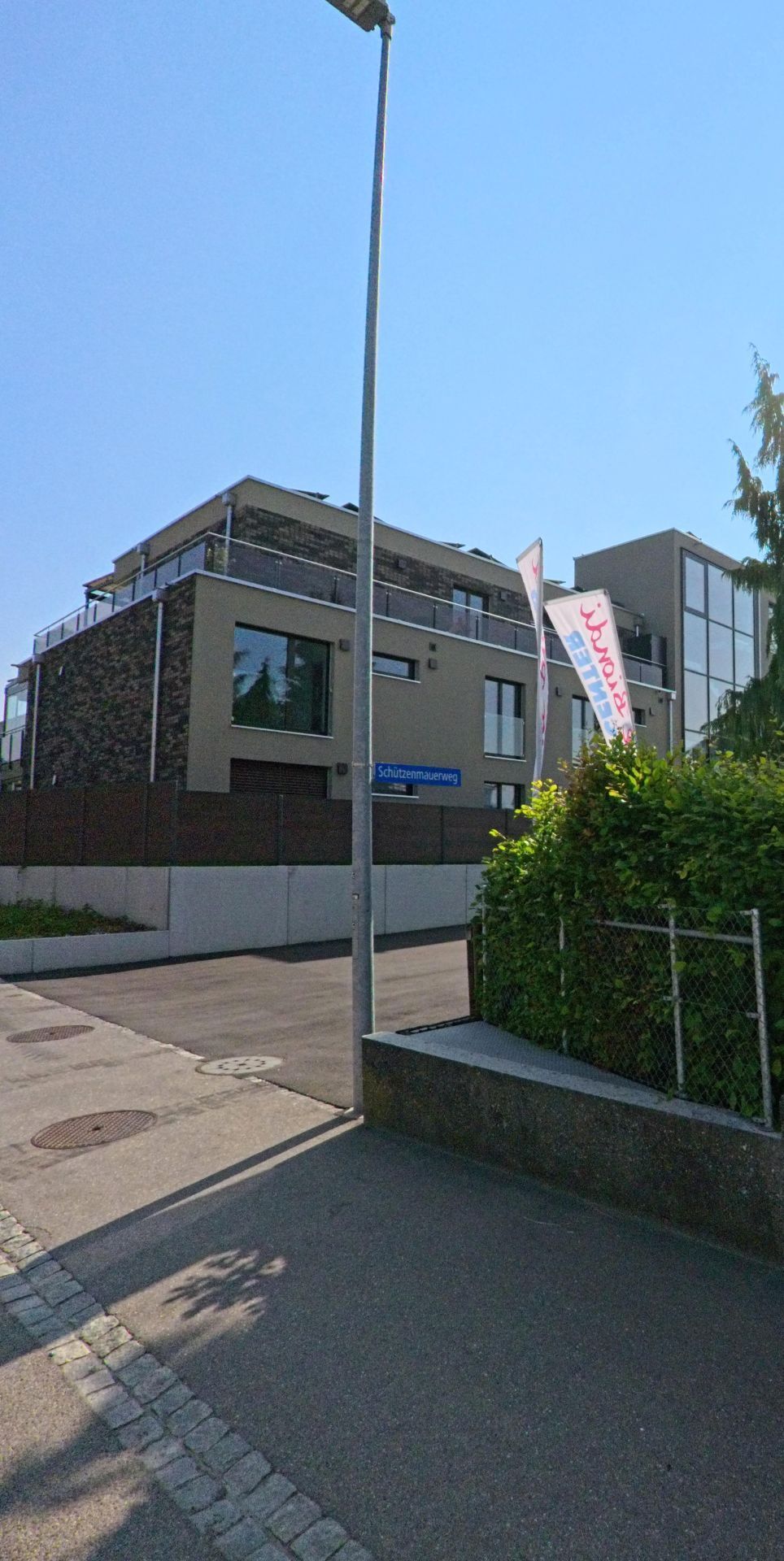Ein modernes Mehrfamilienhaus mit Balkonen steht an einer ruhigen Wohnstrasse in Urtenen-Schönbühl (3322, Kanton Bern) bei klarem Himmel.