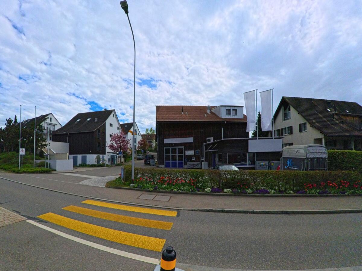 In Uster (8615, Kanton Zürich) liegt ein kleiner Gewerbebetrieb mit Blumenrabatten gegenüber einem gut markierten Fussgängerstreifen.