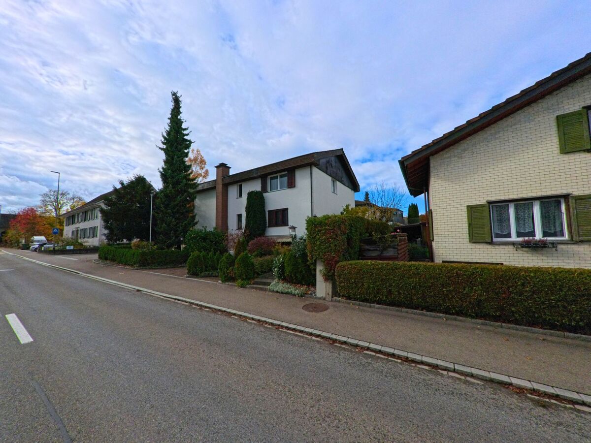 Entlang einer ruhigen Wohnstrasse in Uttwil (8592, Kanton Thurgau) reihen sich gepflegte Einfamilienhaeuser mit Vorgärten und herbstlicher Bepflanzung aneinander.