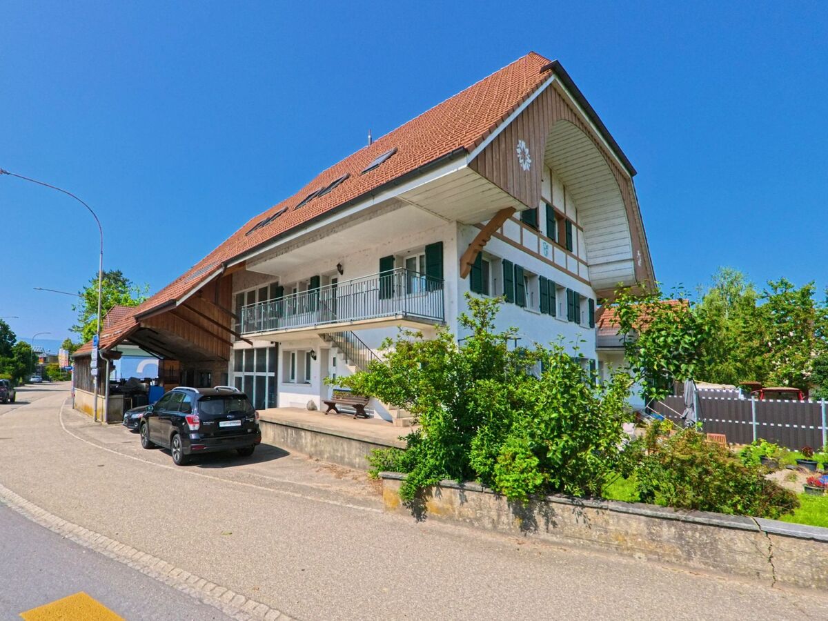 Ein grosses Bauernhaus mit breitem Dachvorsprung und grünen Fensterläden steht in Utzenstorf (3427, Kanton Bern) direkt an einer leicht gebogenen Strasse.