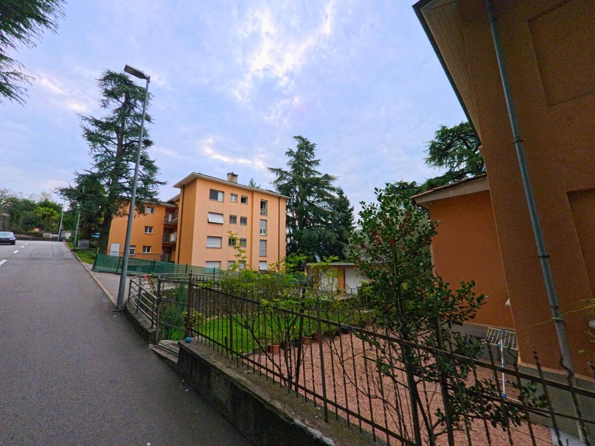In Vacallo (6833, Kanton Tessin) stehen orangefarbene Mehrfamilienhäuser entlang einer leicht ansteigenden Strasse mit Gartenanlagen und Bäumen.