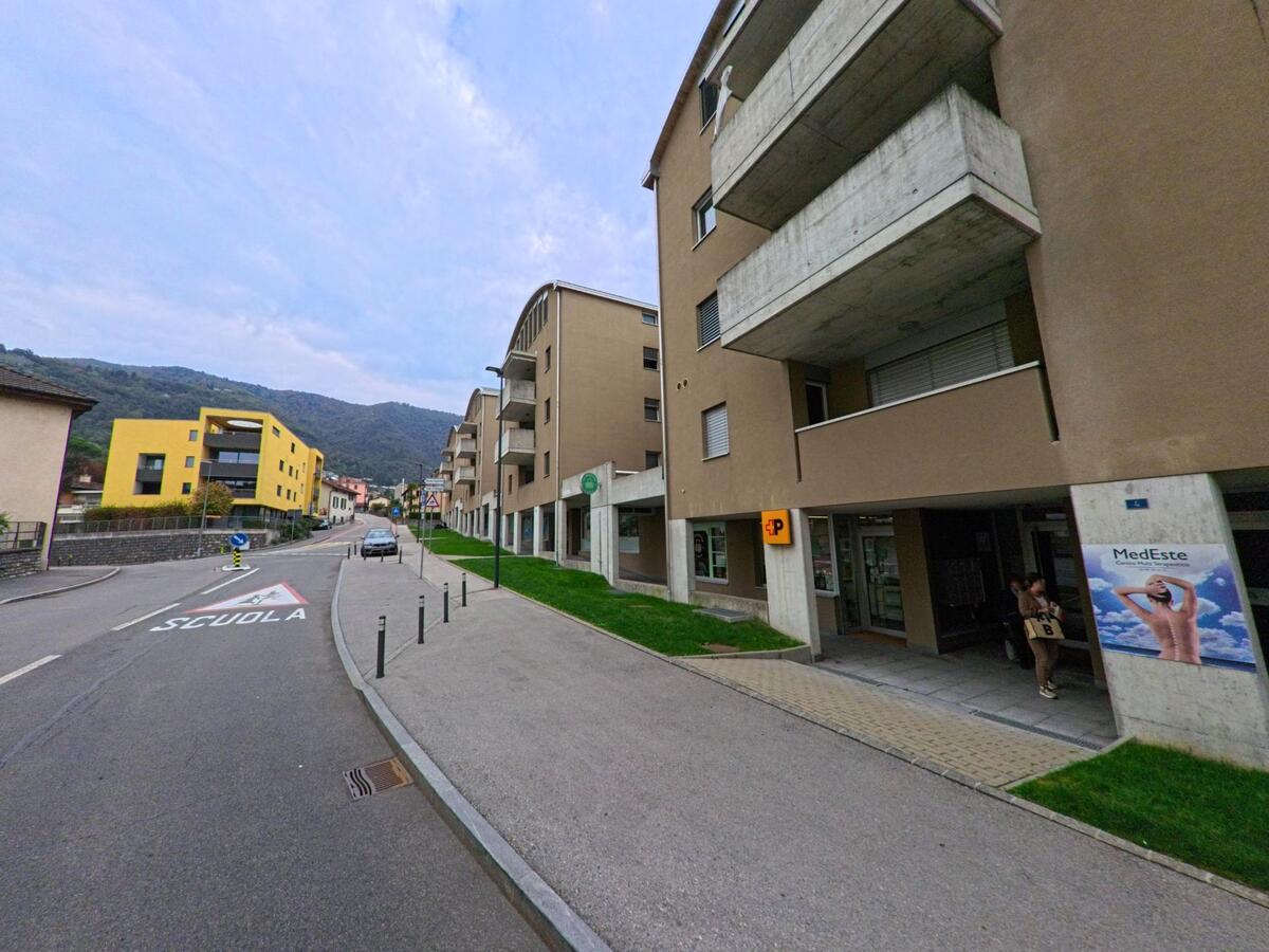 Entlang der Hauptstrasse in Vacallo (6833, Kanton Tessin) stehen moderne Wohnhäuser mit Geschäften im Erdgeschoss und Blick auf die umliegenden Hügel.