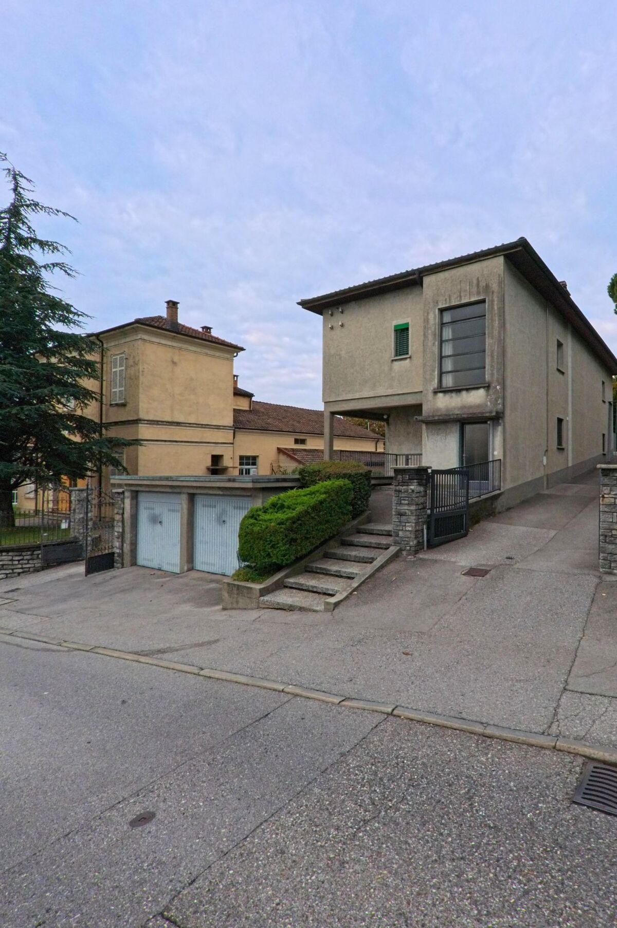 Zwei Wohnhaeuser in Vacallo (6833, Kanton Tessin) liegen nebeneinander, verbunden durch eine gepflasterte Einfahrt mit Garagentoren und gepflegter Hecke.