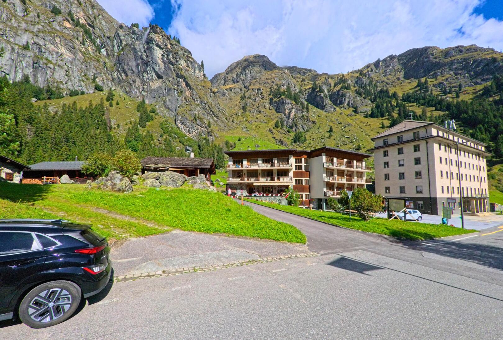 Am Rand einer Bergstrasse stehen Wohn- und Hotelgebaeude vor steilen Felswaenden in Val de Bagnes (1934, Kanton Wallis).