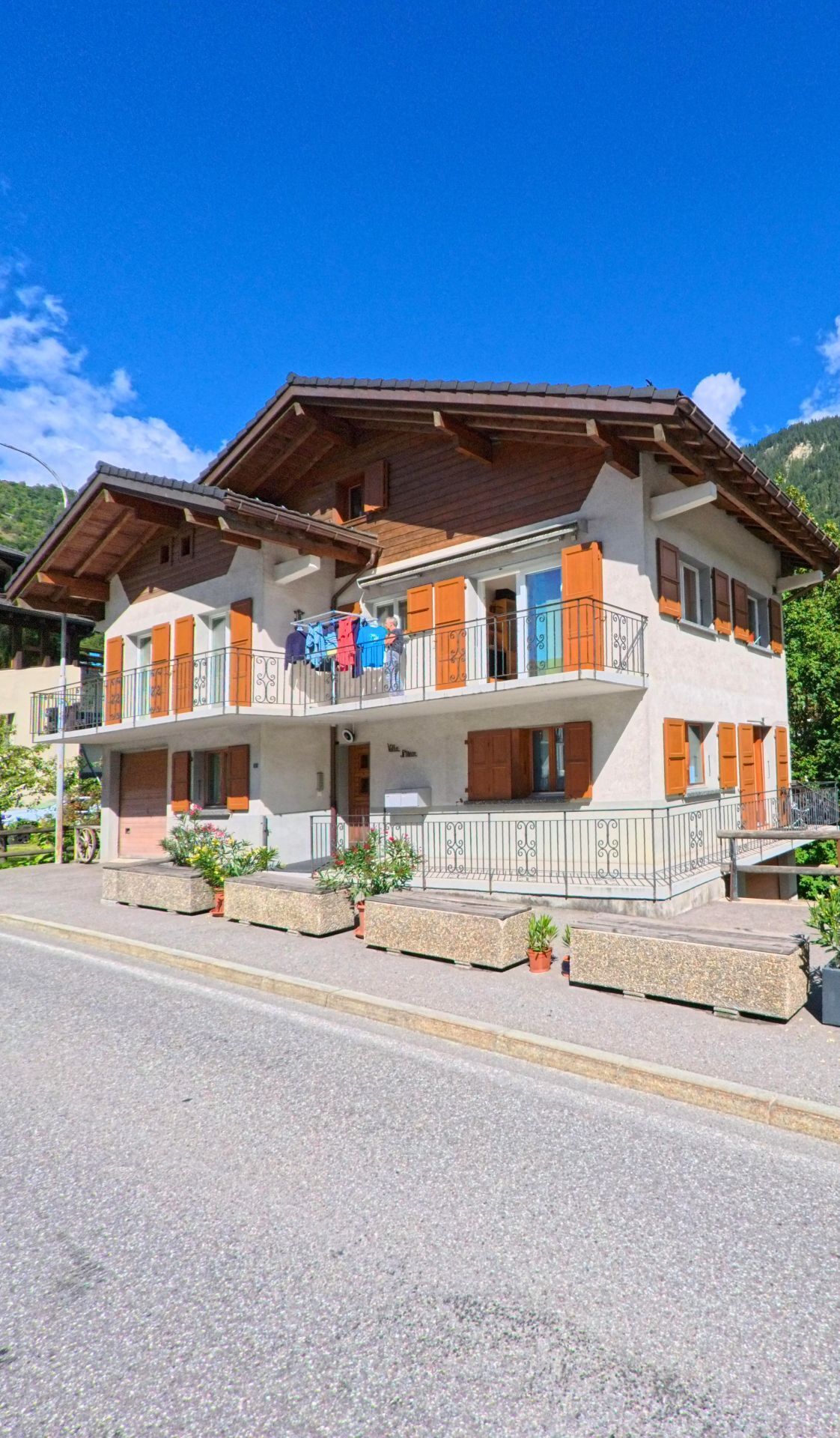 Ein traditionelles Mehrfamilienhaus mit Balkonen und Holzlaeden steht an einer Strasse in Val de Bagnes (1934, Kanton Wallis).