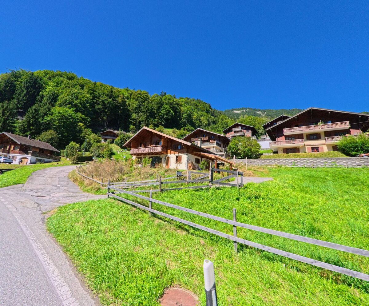 Am sonnigen Hang von Val-d'Illiez (1873, Kanton Wallis) stehen mehrere Chalets, umgeben von grünen Wiesen und dichtem Wald.