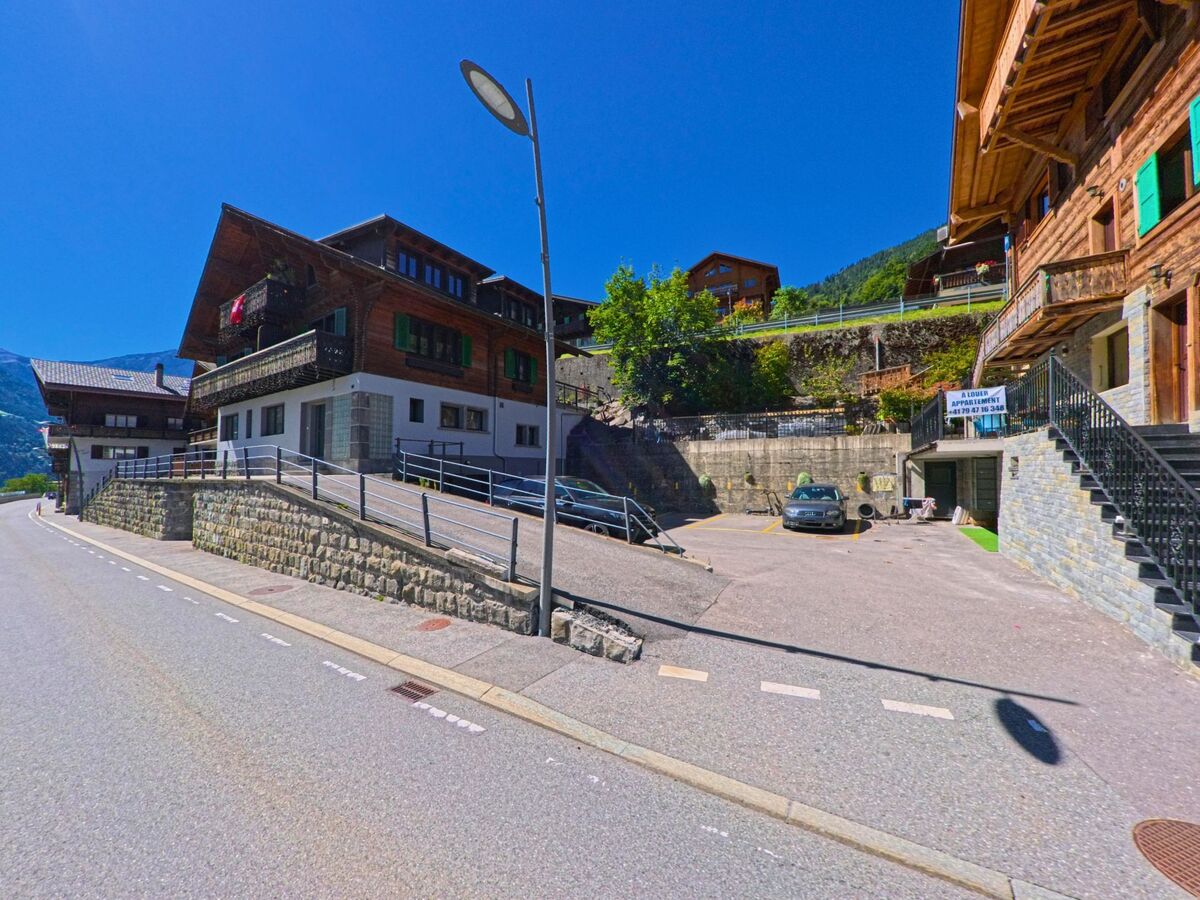 In Val-d'Illiez (1873, Kanton Wallis) stehen mehrere Holzhäuser mit typischen Balkonen entlang einer ruhigen Strasse mit angrenzendem Parkplatz.