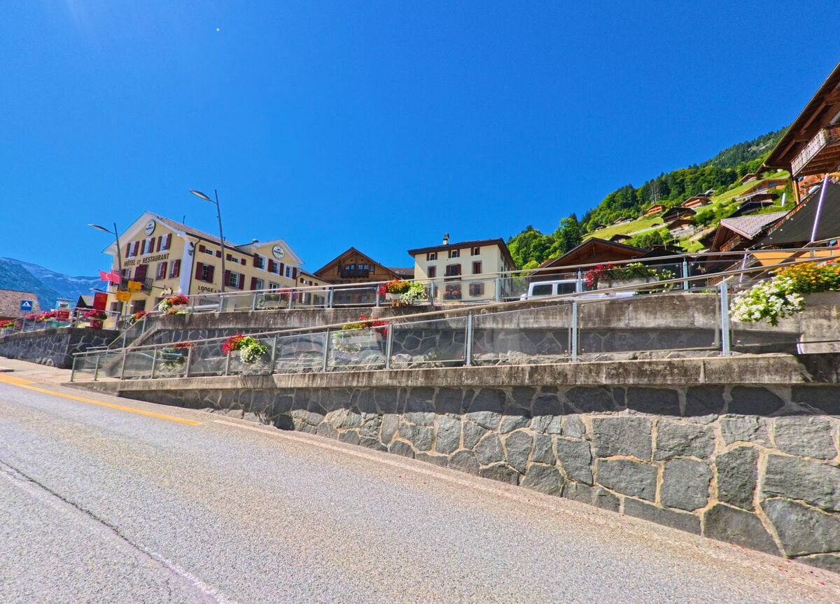 An einer erhöhten Strasse in Val-d'Illiez (1873, Kanton Wallis) reihen sich Häuser und ein Hotel, geschmückt mit zahlreichen Blumenkästen.