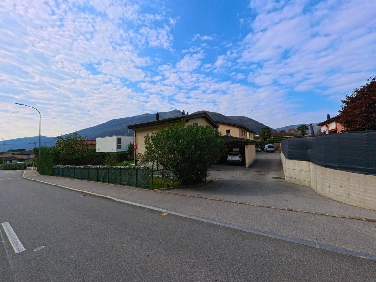 In Val Mara (6818, Kanton Tessin) stehen moderne Einfamilienhaeuser mit Einfahrten und Carports entlang einer ruhigen Strasse mit Blick auf die Berge.