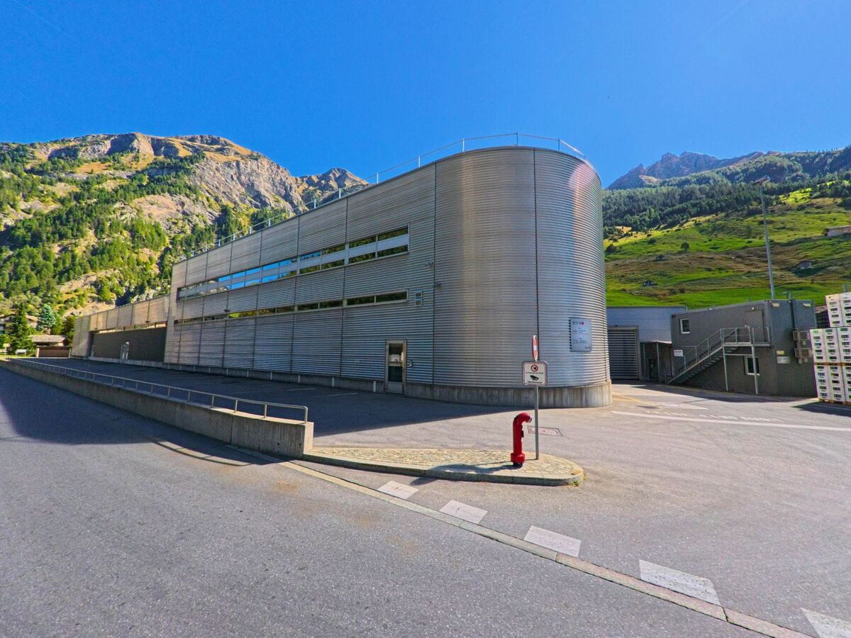 Ein modernes Industriegebäude mit Metallfassade steht in Vals (7132, Kanton Graubünden) vor der Kulisse der grünen Berghänge und Felsen.