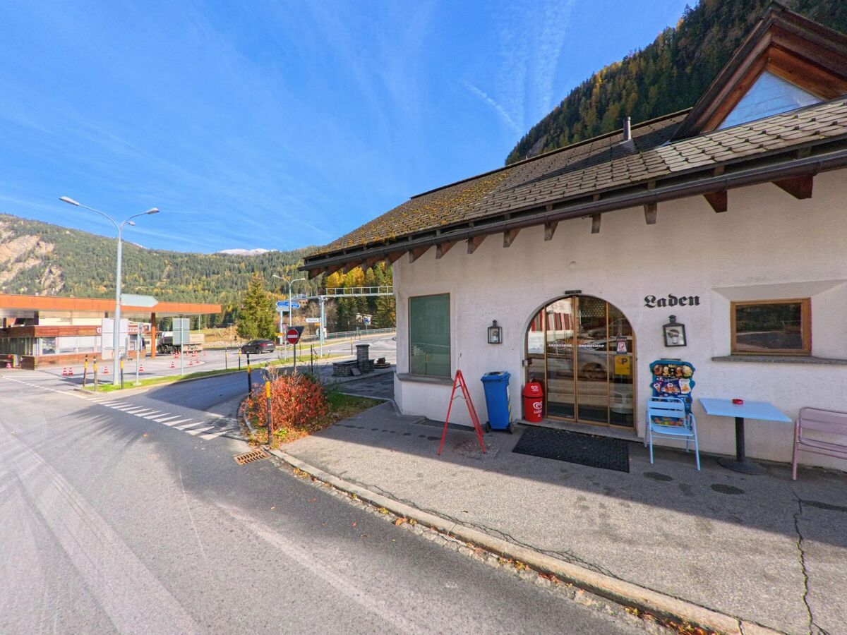 An der Strasse von Valsot (7560, Kanton Graubünden) befindet sich ein kleines Ladenlokal mit überdachtem Eingang, während sich im Hintergrund Verkehrsanlagen und bewaldete Berghänge zeigen.