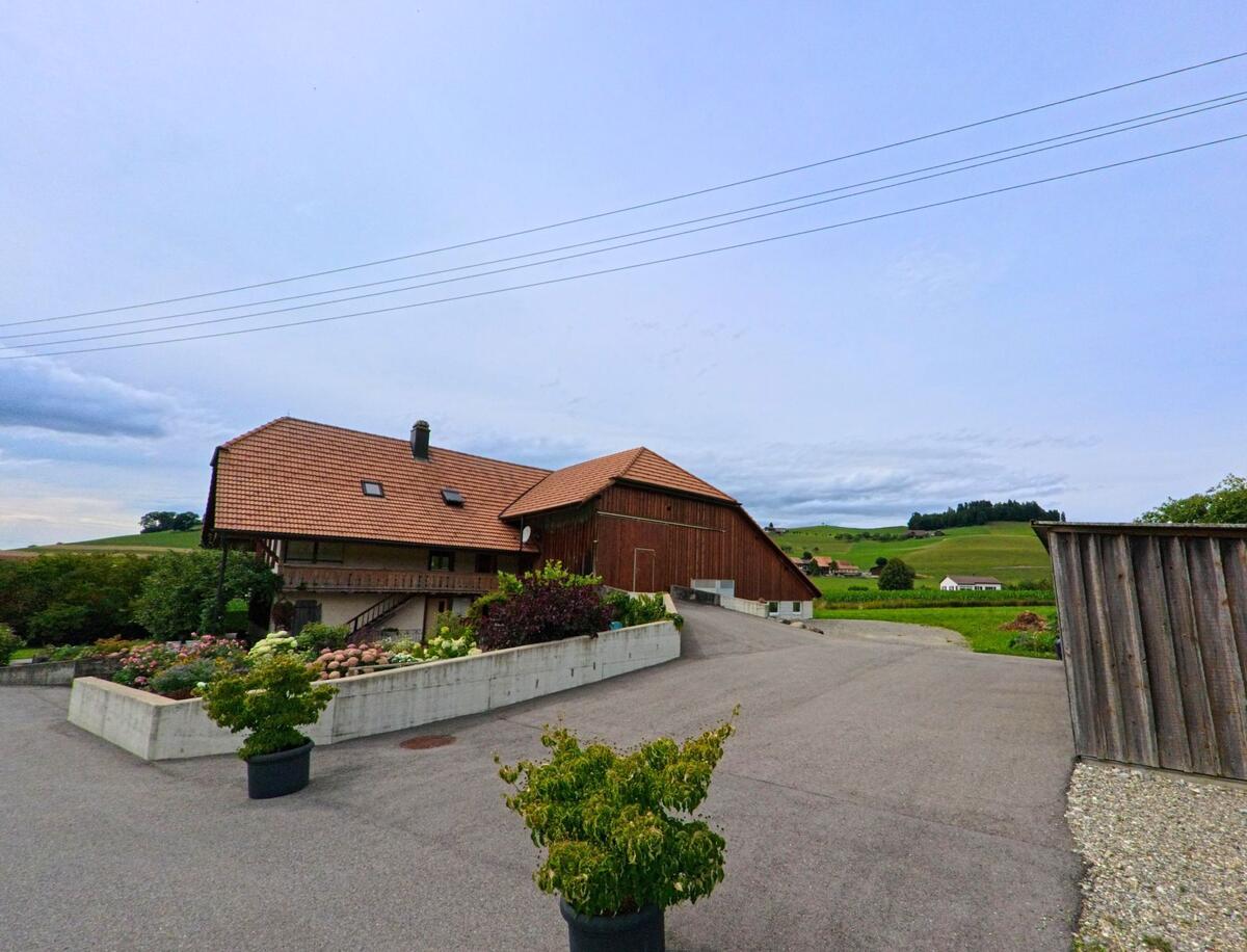 Ein grosser Bauernhof mit Wohnhaus und Scheune steht in Vechigen (3067, Kanton Bern) umgeben von gepflegten Beeten und weiter Landschaft.