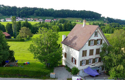 Das Chinderhus Blueme in Grub (9035, Kanton Appenzell Ausserrhoden) befindet sich in einem freistehenden Haus mit Garten, umgeben von grünen Wiesen und Hügeln.