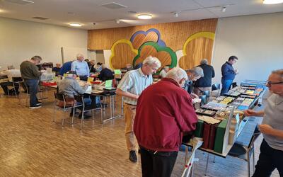 Bei einer Briefmarkenbörse in Aarau (5032, Kanton Aargau) betrachten mehrere Besucher Sammlungen, Alben und Belege an langen Ausstellungstischen.