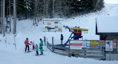 In Kuessnacht am Rigi (6403, Kanton Schwyz) wartet eine Gruppe von Skifahrern am Skilift Seebodenalp, umgeben von verschneiten Hängen und dichten Baumbeständen.