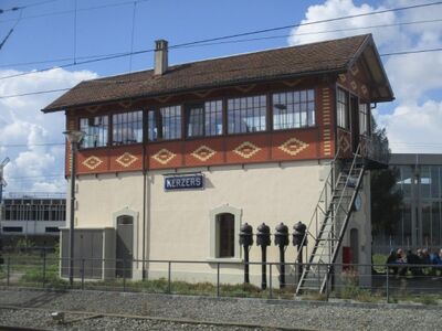 Ein historisches Stellwerkgebaeude mit Beschriftung steht neben Bahngleisen in Kerzers (3210, Kanton Freiburg) und zeigt Eisenbahntechnik.