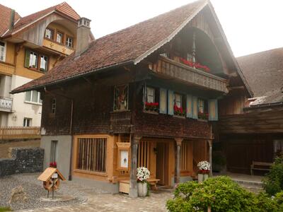 Ein traditionelles Holzhaus mit Balkon, Bluemenkisten und tief gezogenem Satteldach steht in Guggisberg (3158, Kanton Bern) in einem gepflegten Hofbereich.