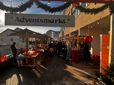 Besucher schlendern am Adventsmarkt in Gallenkappel (8735, Kanton St Gallen) zwischen festlich geschmückten Marktständen in der Abendsonne.