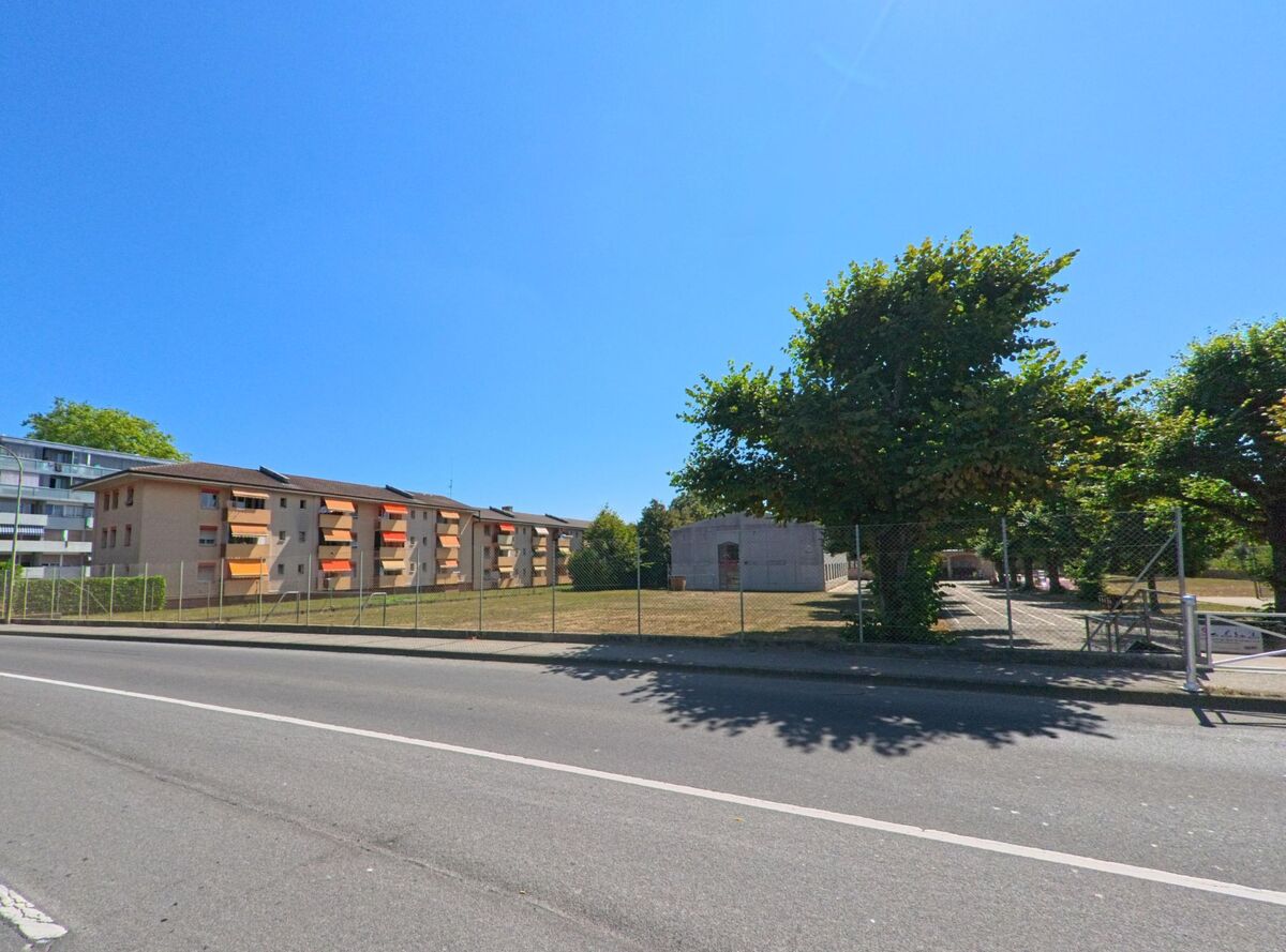 In Vernier (1214, Kanton Genf) stehen Wohngebaeude mit bunten Balkonen neben einer umzauenten Gruenflaeche und einem kleinen Gebaeude.