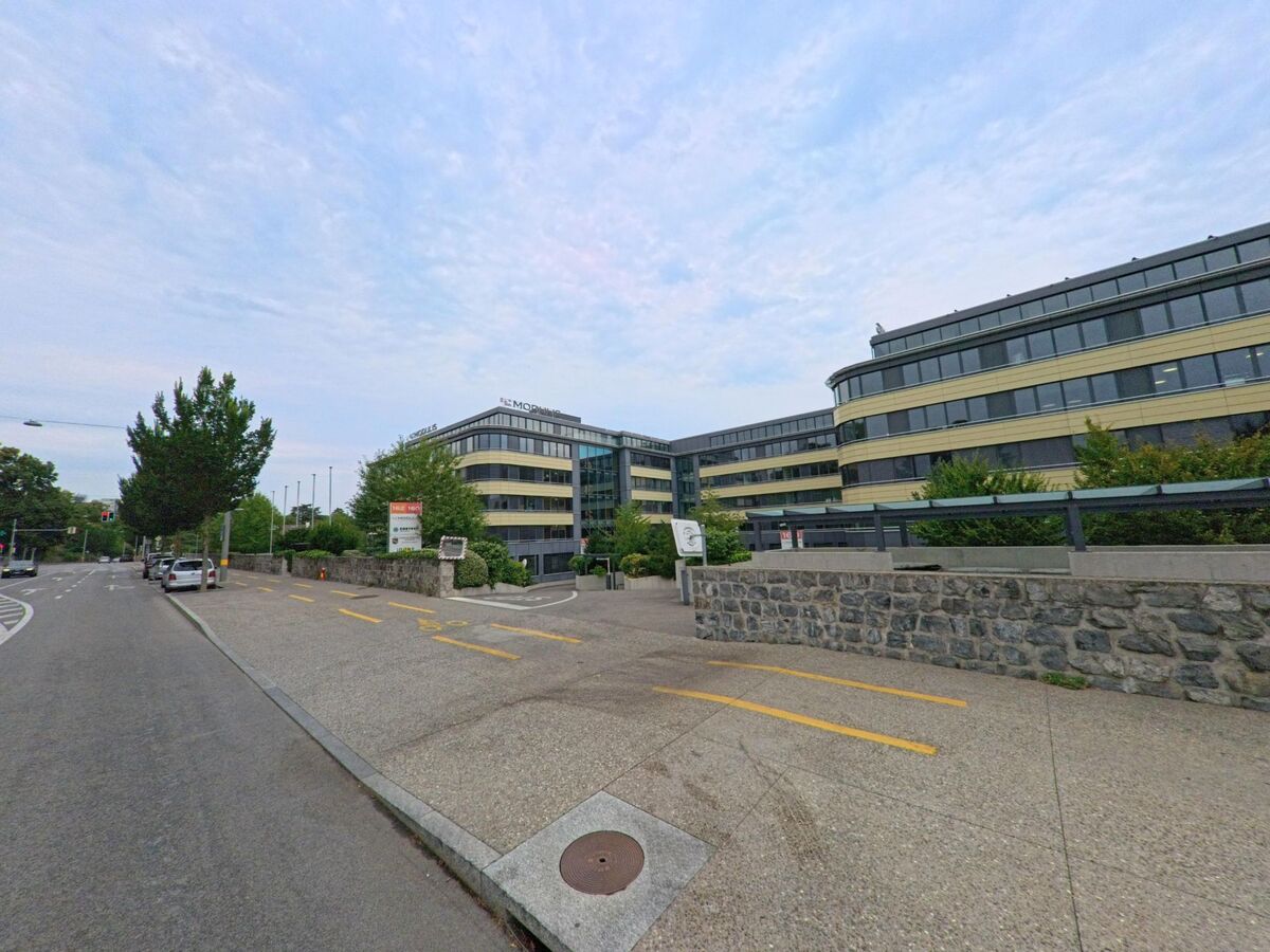 Ein modernes Buero- und Verwaltungsgebaeude mit grossen Glasfronten und geschwungenen Fassaden steht an einer Hauptstrasse in Versoix (1290, Kanton Genf).