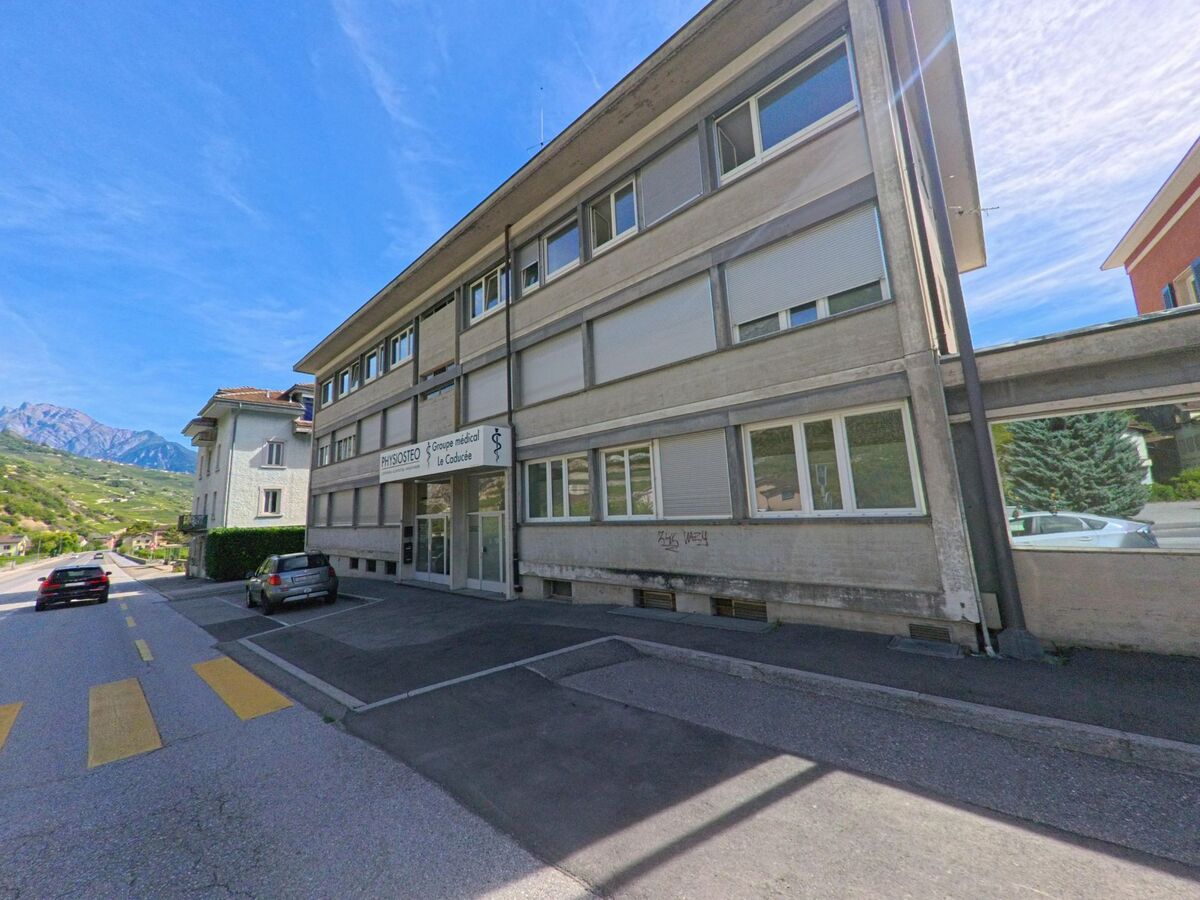 Ein modernes Gebaeude mit Arztpraxis und grossen Fenstern steht in Vetroz (1963, Kanton Wallis) an einer Hauptstrasse.