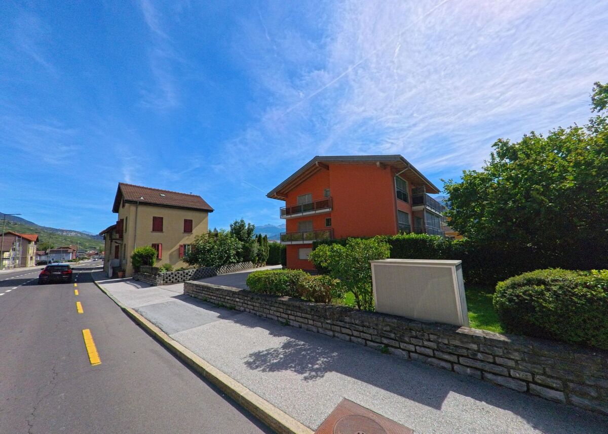 In Vetroz (1963, Kanton Wallis) stehen ein modernes Mehrfamilienhaus und ein traditionelles Wohnhaus an einer ruhigen Strasse.