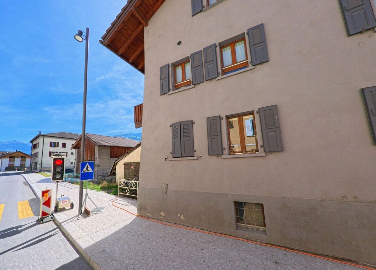 In Vetroz (1963, Kanton Wallis) stehen Wohnhaeuser mit Fensterlaeden entlang einer Strasse mit Baustellenampel.