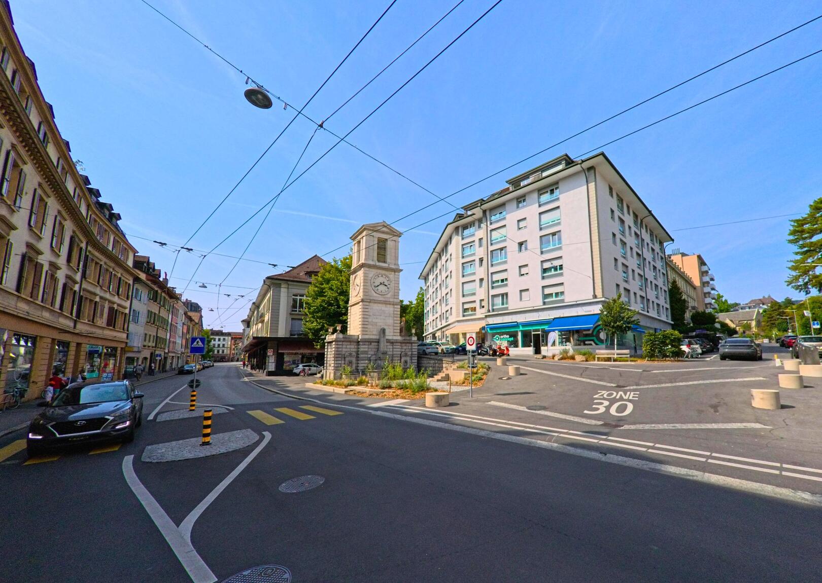 Am Verkehrsknotenpunkt in Vevey (1800, Kanton Waadt) steht ein steinerner Uhrturm zwischen Wohnhaeusern und Geschaeften.