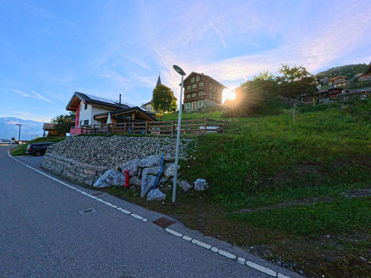 Die Sonne geht hinter den Häusern von Veysonnaz (1993, Kanton Wallis) unter, während ein Kirchturm und mehrere Chalets am Hang sichtbar sind.