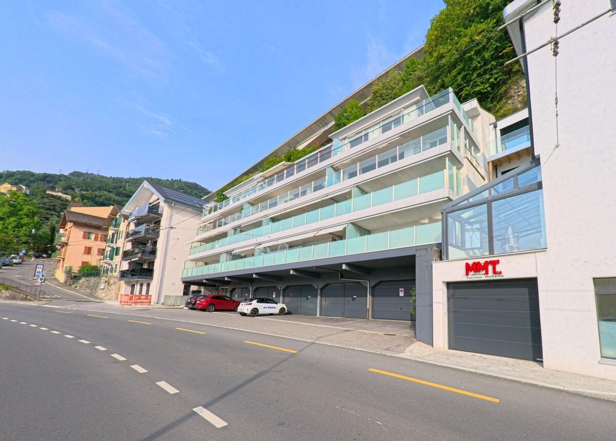 In Veytaux (1820, Kanton Waadt) stehen moderne Wohnhäuser mit grossen Balkonen an einer ansteigenden Strasse unterhalb eines bewaldeten Hangs.