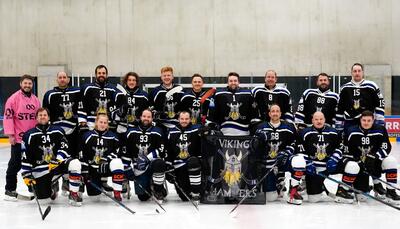 Mannschaftsfoto der Viking Hammers in Dägerlen (8450, Kanton Zürich). Die Eishockeyspieler des Vereins posieren in voller Ausrüstung auf der Eisfläche einer Eishalle und präsentieren ihre schwarzen Teamtrikots sowie das Vereinsbanner in der Bildmitte. Das Gruppenbild zeigt die aktive Mannschaft des Vereins im Kanton Zürich.