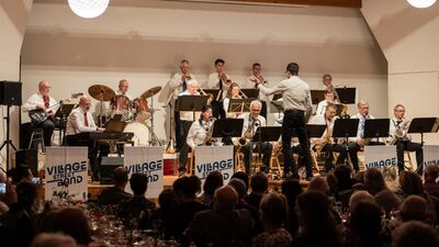 Vor Publikum spielt in Münchenbuchsee [3053] im Kanton Bern eine Band auf der Buehne, waehrend der Dirigent das Ensemble mit erhobenen Armen leitet.