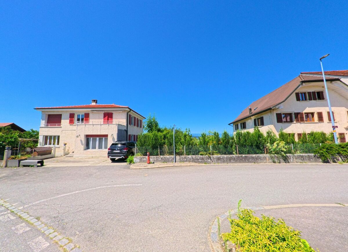 Zwei Wohnhäuser mit roten bzw. braunen Fensterläden stehen sich an einer Strasseneinmündung in Villarzel (1555, Kanton Waadt) gegenüber.