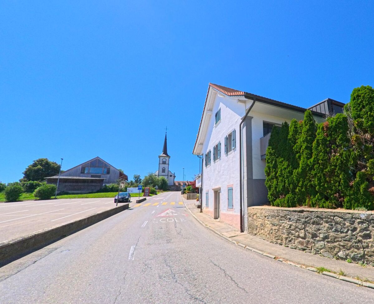 Eine ansteigende Strasse in Villaz (1690, Kanton Freiburg) führt an Wohnhäusern vorbei zur Kirche mit markantem Turm.