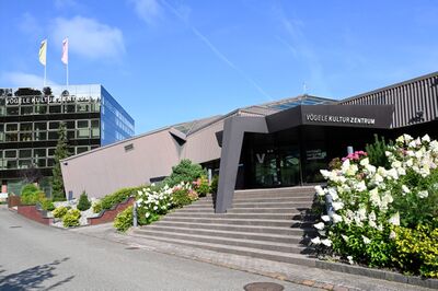 Das Vögele Kultur Zentrum in Pfäffikon SZ (8808, Kanton Schwyz) zeigt eine moderne Architektur mit Glasfassade und blühenden Gartenanlagen.