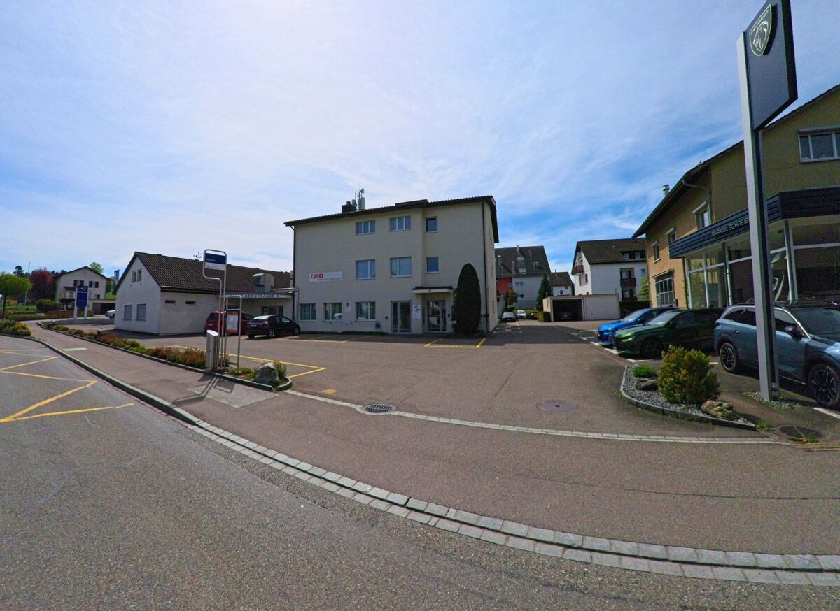 In Volketswil (8604 im Kanton Zürich) liegt eine Bushaltestelle vor einem Gewerbegebäude an einer breiten Strasse mit angrenzendem Autohaus.