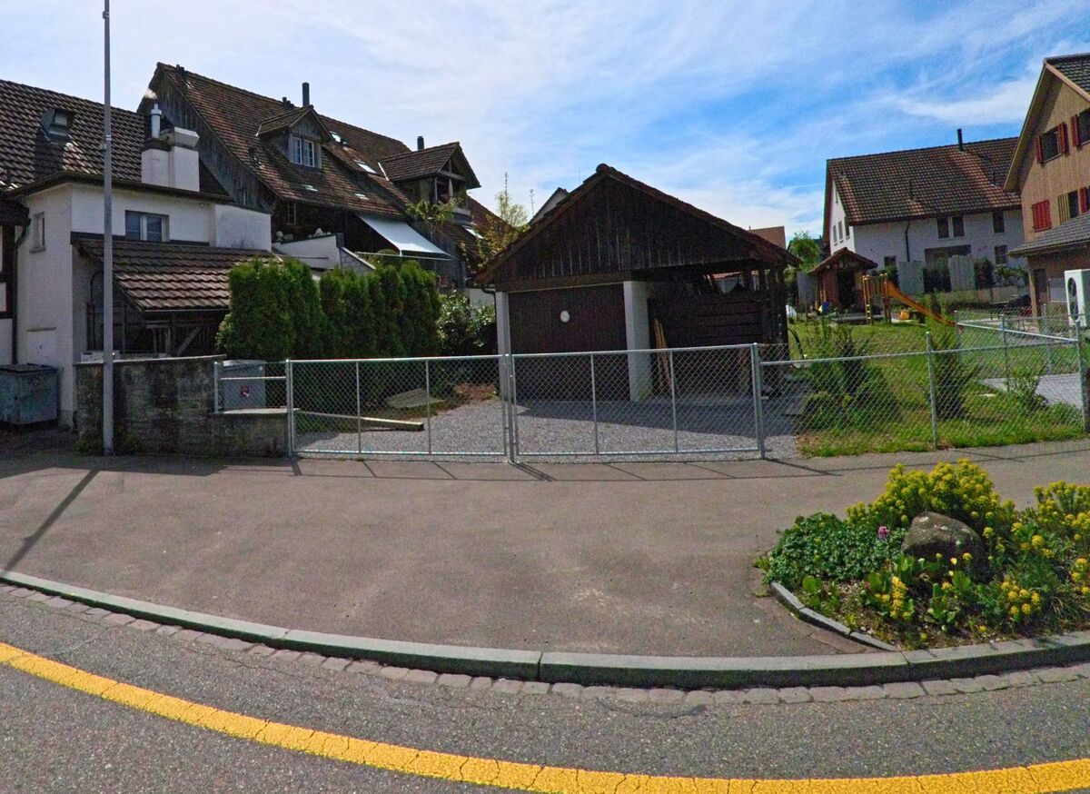 In Volketswil (8604 im Kanton Zürich) markiert ein Zebrastreifen den Übergang zwischen einem Fachwerkhaus und einem Wohnquartier, während im Hintergrund ein Baukran sichtbar ist.