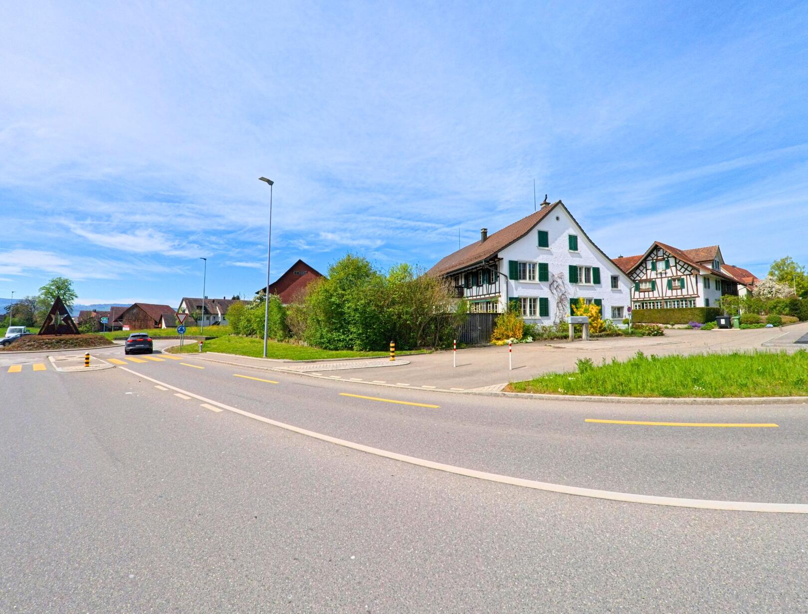 In Volketswil (8605 im Kanton Zürich) stehen zwei traditionelle Häuser mit grünen Fensterläden und Fachwerk nahe eines Kreisverkehrs mit markanter Sternskulptur.