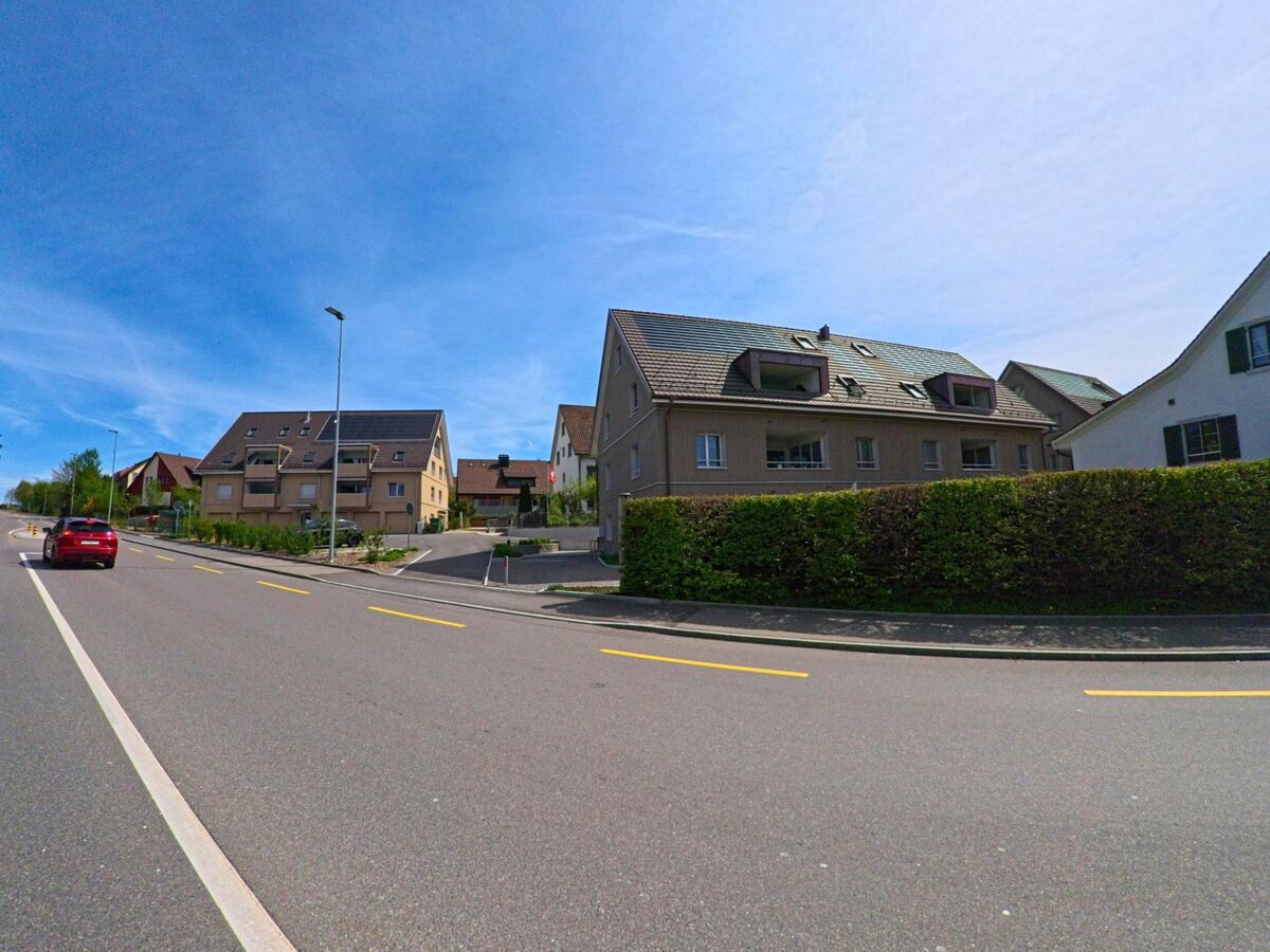 In Volketswil (8605 im Kanton Zürich) verlaufen moderne Wohnbauten entlang einer sanft ansteigenden Hauptstrasse mit gut markierten Fahrspuren und Randbepflanzung.