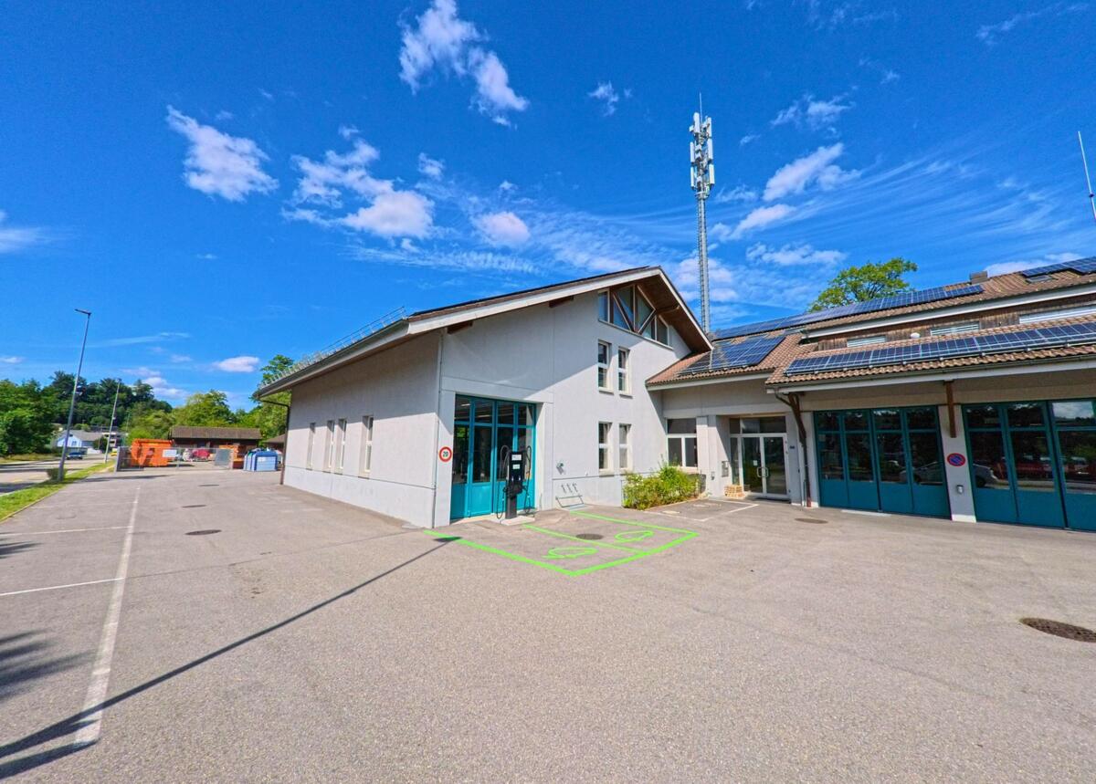 Ein modernes Betriebsgebaeude mit Photovoltaikanlage und E-Ladestation steht in Vordemwald (4803, Kanton Aargau) am Rand eines weitlaeufigen Parkplatzes.