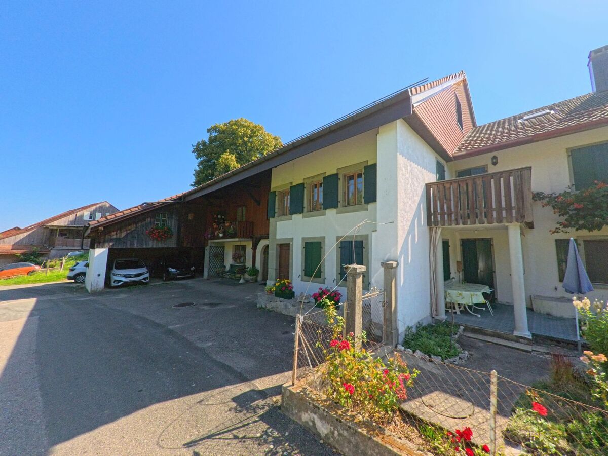 Ein traditionelles Wohnhaus mit Balkon und Blumenschmuck steht in Vucherens (1509, Kanton Waadt) neben einem kleinen Hofbereich.