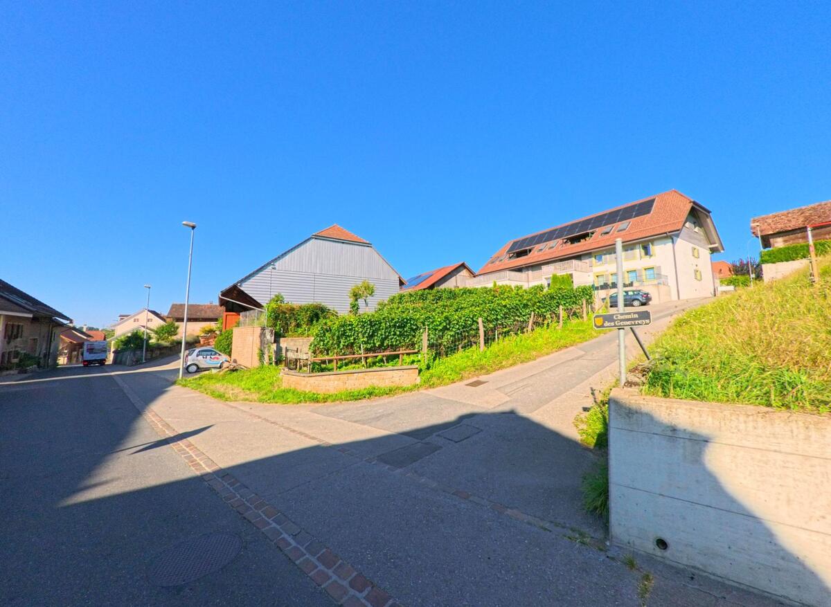 In Vully-les-Lacs (1586, Kanton Waadt) fuehrt eine Strasse an einem Haus mit grossen Solarpanelen und gelben Fensterlaeden vorbei, waehrend ein Wegweiser den Chemin des Genevreys anzeigt.