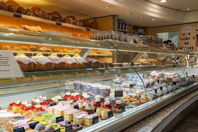 Eine beleuchtete Verkaufstheke in einer Bäckerei in Rothrist (4852, Kanton Aargau) zeigt Torten, Gebäck und Brotlaibe hinter Glas