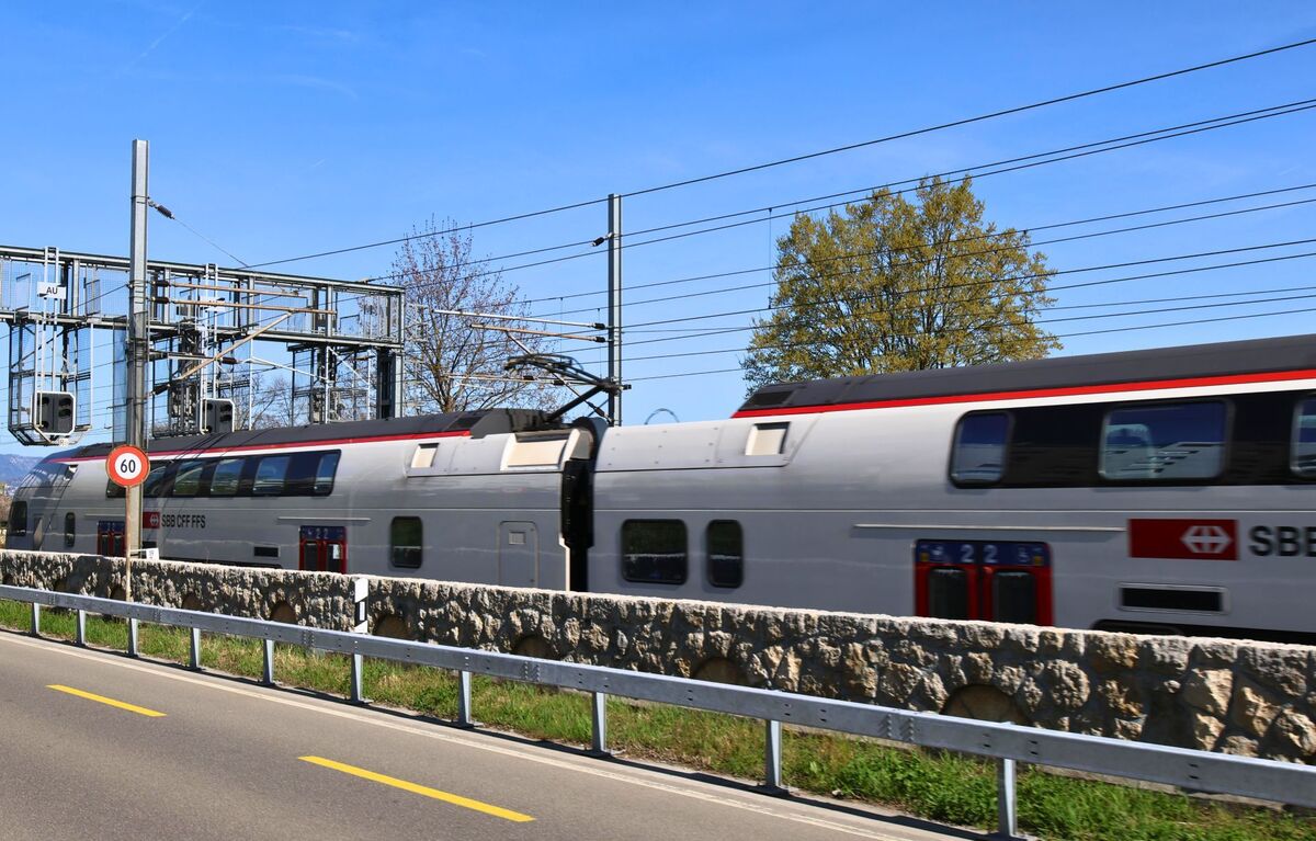In Wädenswil (8820 im Kanton Zürich) fährt ein doppelstöckiger SBB-Zug an einer parallel verlaufenden Strasse vorbei, getrennt durch ein historisches Natursteinmauerwerk.