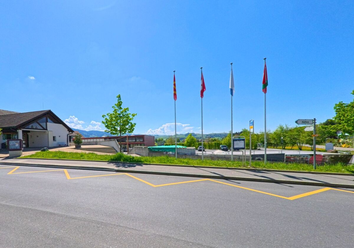 In Wädenswil (8824, Kanton Zürich) stehen mehrere Fahnen vor einem öffentlichen Gebäude mit moderner Architektur und Blick auf die umliegende Hügellandschaft.