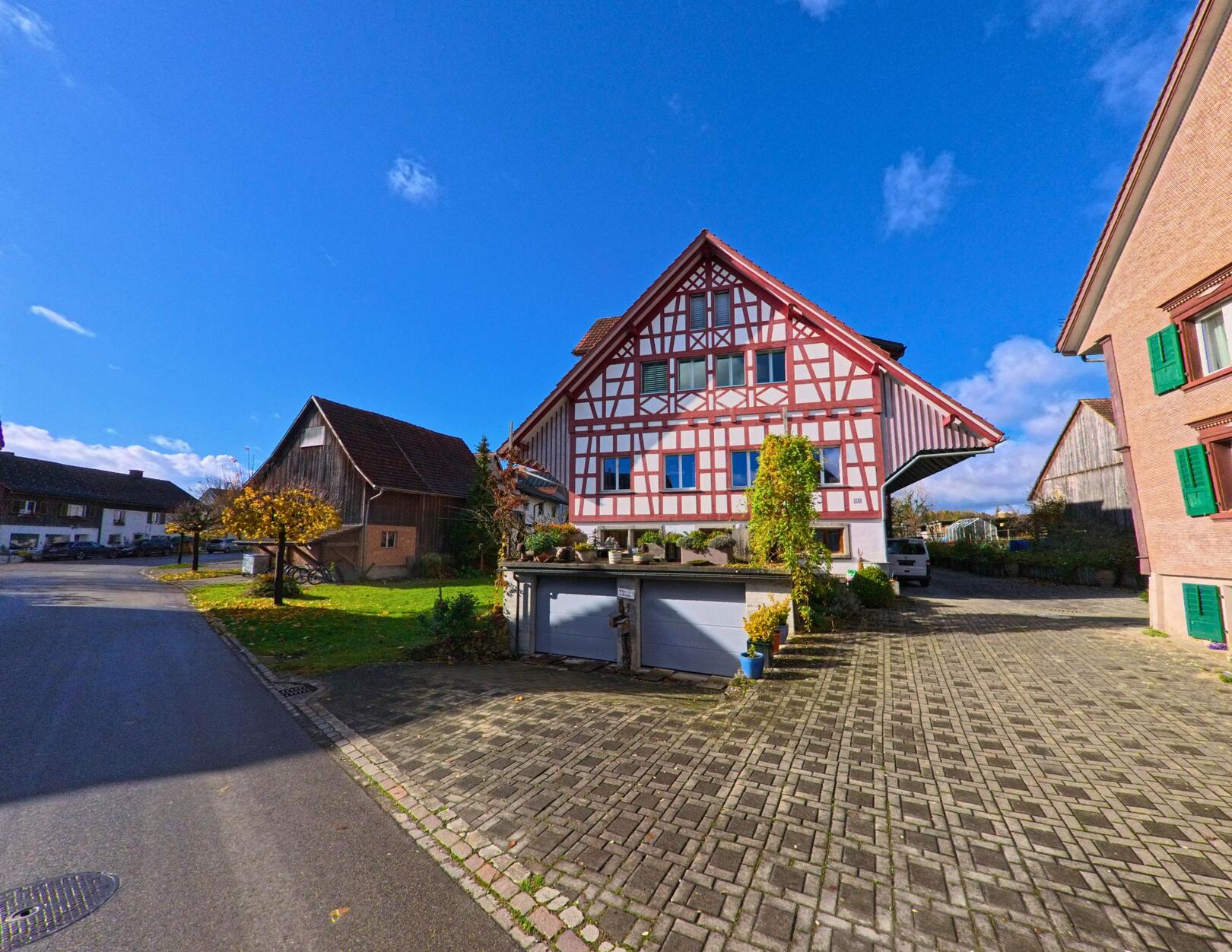 Ein traditionelles Fachwerkhaus mit gepflastertem Vorplatz und angrenzender Dorfstrasse prägt das Ortsbild von Wäldi (8564, Kanton Thurgau) unter blauem Himmel.