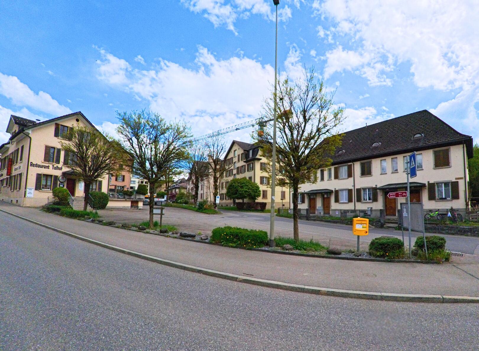 In Wald (8636, Kanton Zürich) liegt ein kleiner Platz mit Bäumen und Sitzbänken zwischen traditionellen Wohnhäusern und einem Restaurant.