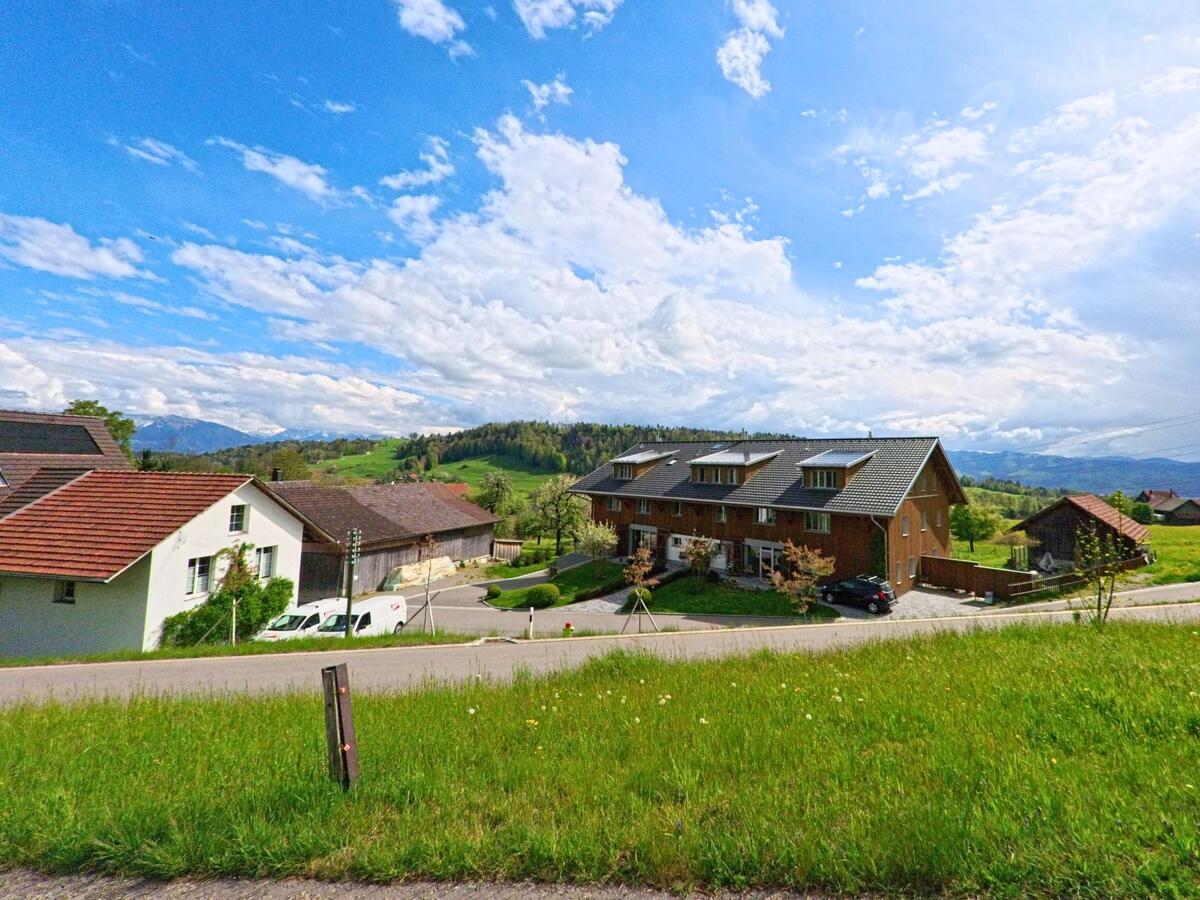 In Wald (8663, Kanton Zürich) reihen sich Ein- und Mehrfamilienhäuser entlang einer Landstrasse mit Blick auf die hügelige Voralpenlandschaft.