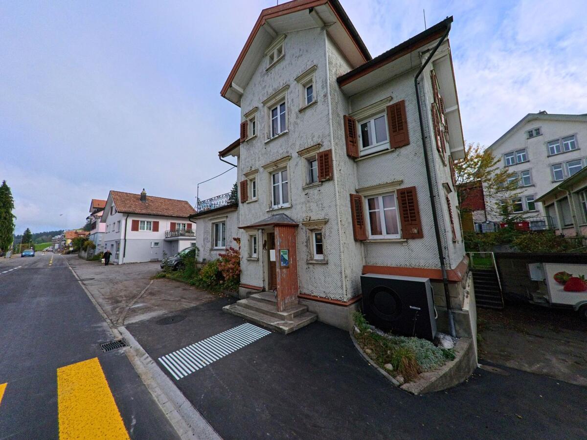 An der leicht ansteigenden Strasse in Wald (9044, Kanton Appenzell Ausserrhoden) steht ein traditionsreiches Wohnhaus mit braunen Fensterlaeden und kleinem Vorgarten.