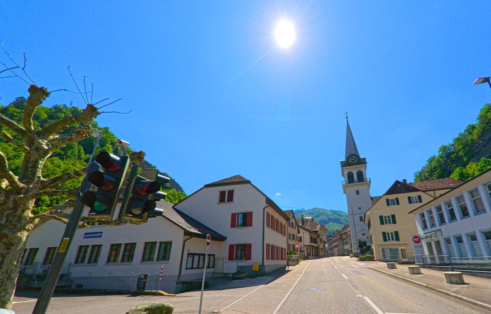 In Waldenburg (4437, Kanton Baselland) zeigt sich die Hauptstrasse bei Sonnenschein mit Blick auf die reformierte Kirche und umgebende Häuserfassaden.